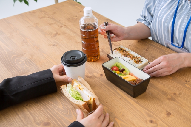 会社員が昼食を食べている様子。お弁当と、サンドイッチを持っている。