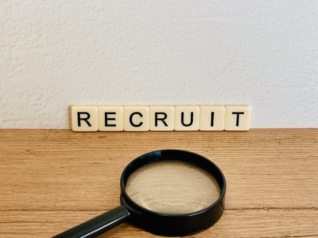 RECRUITと書かれたブロック、虫眼鏡が机の上においてある写真。